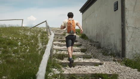 Hiker-with-an-orange-baackpack-running-up-the-stairs-on-path-to-the-top-of-mountain-Slavnik-past-the-cottage