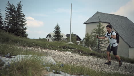 Camera-tracking-a-hiker-walking-with-hiking-poles-up-a-rocky-path-past-the-church-at-the-top-of-mountain-Uršlja-gora