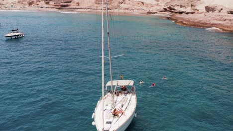 People-swimming-next-to-moored-white-sailing-yacht-at-Tenerife,-aerial
