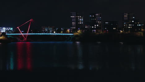 Nachtansicht-Der-Fußgängerbrücke-Im-Pae-Park,-Beleuchtet-Mit-Buntem-Licht-über-Dem-Seewasser-Mit-Gebäuden-Im-Hintergrund,-Tallinn,-Estland
