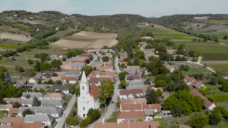 Flying-over-a-small-town,-with-a-catholic-church,-agricultural-land-around,-and-a-forest