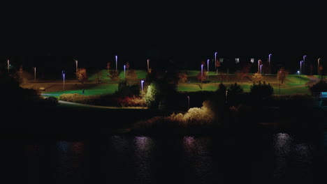 Person-walking-at-Pae-park-alongside-pond-illuminated-with-night-light,-Tallinn,-Estonia