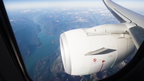 Wide-shot-of-plane-engine-and-wing-in-flight-with-mountains-and-lake-in-background