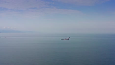 Passenger-airplane-flying-over-Black-sea-expanse-and-touching-down-at-the-airport-among-Batumi-morning-cityscape