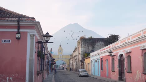 Flock-of-birds-joyfully-flies-around-the-skies-around-the-Santa-Catalina-yellow-clocktower-arch-in-Antigua,-Guatemala