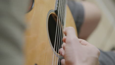 Close-up-slow-motion-footage-of-a-man's-fingers-strumming-on-an-acoustic-guitar-in-a-studio