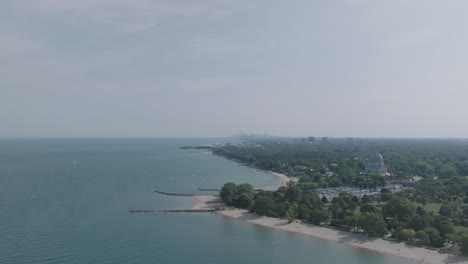 Breite-Luftaufnahmen,-Die-Sich-Von-Der-Küste-Des-Michigansees-Fortbewegen,-Mit-Dem-Baháʼí-haus-Der-Anbetung-Im-Vordergrund-Und-Chicago-Im-Verschwommenen-Hintergrund