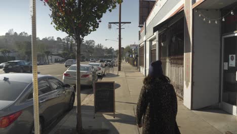Hipster-girl-walking-down-sidewalk-in-urban-area,-dolly-crane-shot