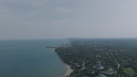 Breite-Luftaufnahmen-Der-Küste-Des-Michigansees-Mit-Dem-Baháʼí-Gotteshaus-Im-Vordergrund-Und-Chicago-Im-Dunstigen-Hintergrund