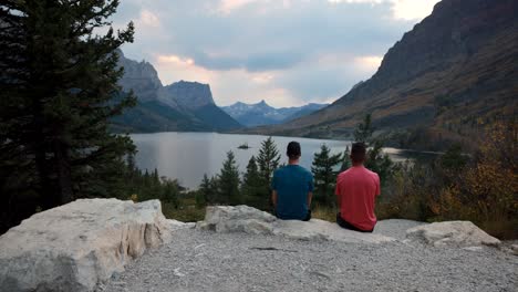 Glacier-National-Park,-Montana-USA---Time-Lapse-with-2-people-sitting-on-a-rock-as-the-clouds-and-tourist-come-to-photograph-St-Mary-lake-and-wild-good-Island