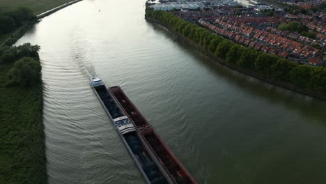 Aerial-footage-of-long-cargo-ship-transporting-bulk-material-in-barges-on-river-in-flat-landscape