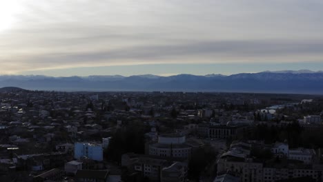Aerial-flying-over-Kutaisi-city-with-snowy-mountains-and-river-Georgia-Country