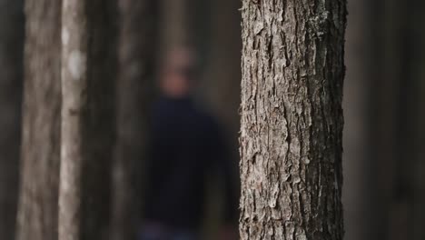 Out-of-focus-male-figure-walks-in-slow-motion-through-the-background-of-a-dimly-lit-forest