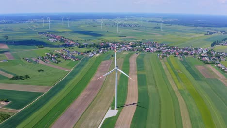 Wide-aerial-pan-of-wind-turbines-by-crop-fields-and-small-town,-Poland