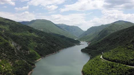 Aerial-view-of-a-wide-river-flowing-through-a-stunning,-green-valley-on-calm-day