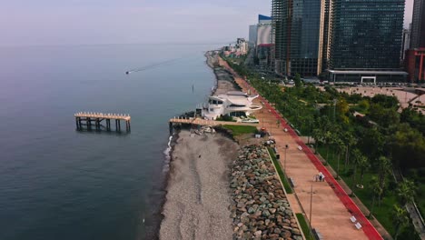 Black-sea-beach-alongside-city-promenade-with-modern-apartment-buildings-and-skyscrapers