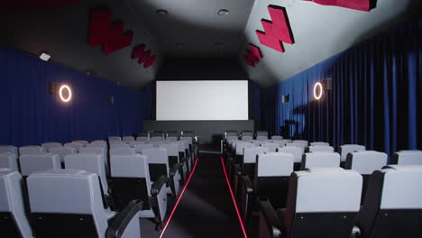 Schieben-Sie-Den-Gang-An-Den-Sitzplätzen-Im-Kinosaal-Vorbei-Und-Blicken-Sie-Auf-Die-Große-Leinwand-Des-Projektors,-4k