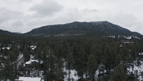 Rising-aerial-shot-through-trees-and-snow-covered-ground-to-reveal-a-mountain-in-northern-Arizona