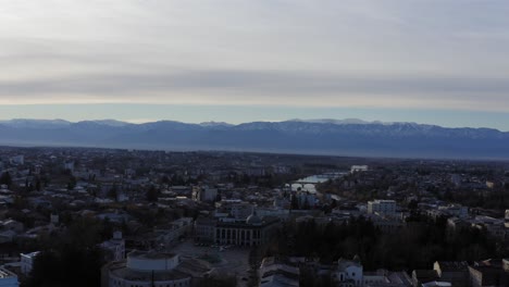 Aerial-flying-over-Kutaisi-city-with-snowy-mountains-and-river-Georgia-Country