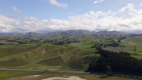 Birds-eye-view-of-a-rural-highway-winding-through-the-lush,-green-hills-of-Marlborough,-New-Zealand-under-a-bright-sunny-sky