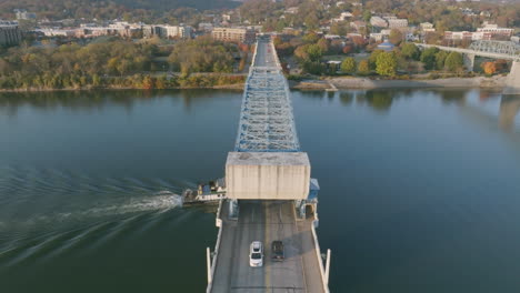 Aerial-footage-following-a-tug-boat-that-is-sailing-under-a-bridge-in-downtown-Chattanooga-on-the-Tennessee-River-during-sunset