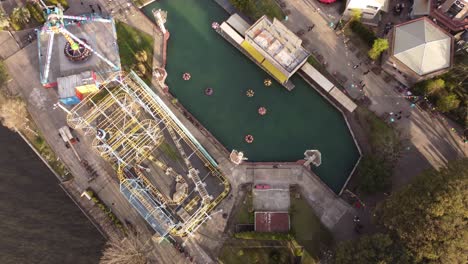 A-dynamic-orbital-aerial-shot-of-the-rollercoaster,-frisbee,-and-bumper-boat-ride-in-action-at-the-Parque-de-la-Costa-amusement-park-in-Tigre,-Buenos-Aires