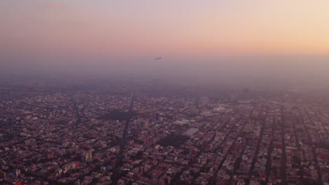 Beautiful-aerial-footage-of-commercial-airplane-landing-at-golden-hour-in-Mexico-City,-smog-glowing-in-the-evening-light
