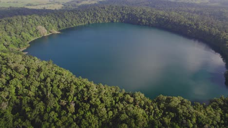 Lago-Eacham-Rodeado-De-Vegetación-Verde-En-Atherton-Tableland,-Queensland,-Australia---Toma-Aérea-De-Drones