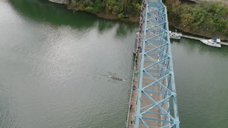Aerial-shot-of-rowers-going-underneath-the-Walking-Bridge-in-downtown-Chattanooga-during-a-race