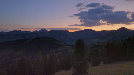 Pull-back-over-trees-and-away-from-mountain-range-just-past-sunset-in-the-Colorado-Rocky-Mountains