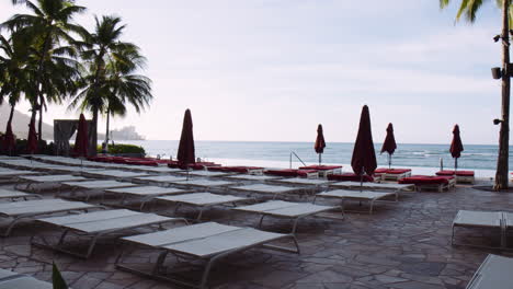 Luxury-Sunbeds-With-Parasols-on-Stone-Terrace-by-Infinity-Pool,-Waikiki-Beachfront,-Hawaii,-Wide-Shot