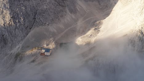 Aerial-through-clouds-revealing-a-rifugio,-small-body-of-water-in-valley