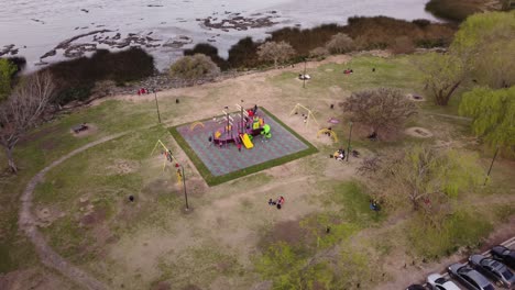 Eine-Dynamische-Orbitale-Luftaufnahme-Von-Kindern,-Die-Auf-Dem-Kinderspielplatz-Mit-Schaukeln-Und-Einer-Von-Einem-Segelschiff-Entworfenen-Kinderrutsche-In-Der-Mitte-Spielen