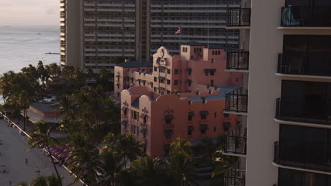 Royal-Hawaiian's-Historic-Beachfront-Resort-with-Palm-Trees,-Sunlight-and-Reflections-on-Waikiki-Beach,-Hawaii