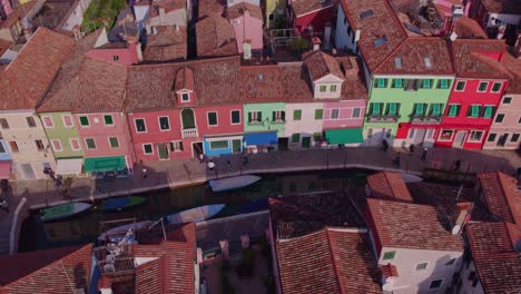 Vibrant-colorful-houses-in-Burano-with-small-canal-and-people-walking,-aerial