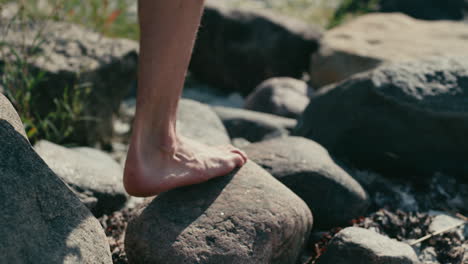 Man-walking-barefoot-on-rocks-close-to-beach,-close-up