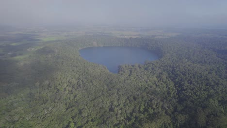 Lake-Eacham-And-Its-Lush-Rainforest-During-A-Misty-Day-In-Atherton-Tableland,-Queensland,-Australia---aerial-drone-shot
