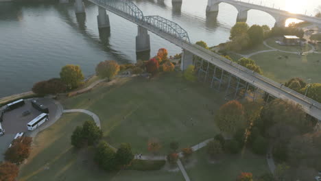 Aerial-footage-of-Coolidge-Park-that-pans-up-and-reveals-the-sunset-shining-over-downtown-Chattanooga,-TN