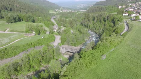 Drone-shot-of-idyllic-landscape-with-green-forest-trees,-flowing-river-and-small-village-between-mountains-in-summer---Fiemme-Valley,Italy