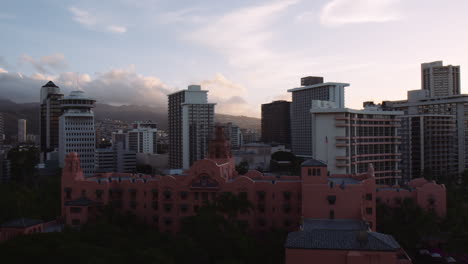 Rosa-Hotelresort-Mit-Hintergrundbeleuchtung-Bei-Sonnenaufgang,-Innenstadt-Von-Waikiki-Im-Hintergrund,-Hawaii