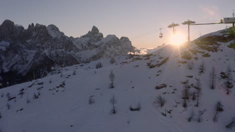 Aerial-forward-flight-showing-ski-lift-and-beautiful-snowy-mountain-range-with-sunset-in-background