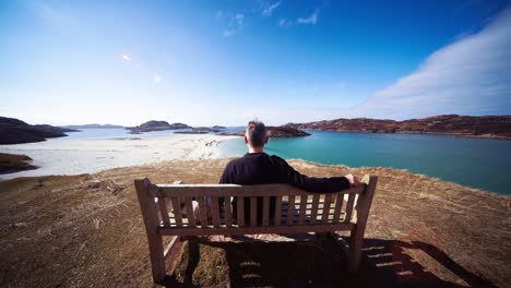Wide-rear-view-of-man-sitting-on-a-bench-enjoying-view,-Erraid-island,-Scotland