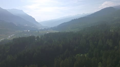 Aerial-view-of-beautiful-Val-di-Fiemme-with-forest-trees-and-mountains-range-in-background-during-sunny-and-foggy-day