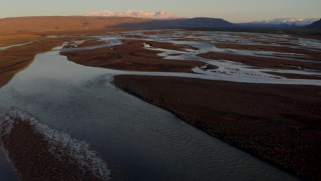 Pan-up-aerial-shot-over-Icelands-braided-rivers-towards-Highland-Mountains