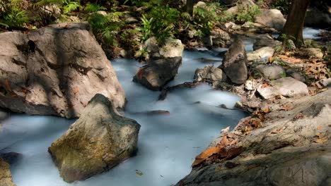 Sulphuric-stream-with-white,-milky-hot-water-flowing-through-a-rocky-river-in-remote-forest-in-Timor-Leste,-Southeast-Asia