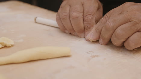 Close-up-slow-motion-footage-of-old-weathered-hands-cutting-a-roll-of-dough-to-make-pasta-shells