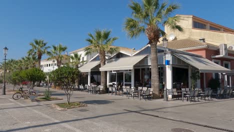 Pan-from-sunny-Restaurant-terraces-to-promenade,-Preveza,-Greece