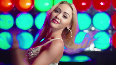 Woman-with-blonde-hair-and-a-sparkly-top-dancing-in-a-colourful-club