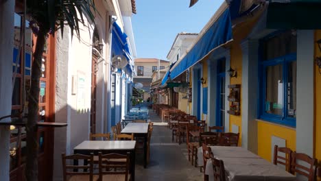 Empty-eating-tables-outside-a-white-building-with-blue-and-yellow-colors-in-Preveza,-Greece