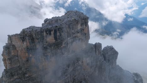 Aerial-oribiting-shot-of-rocky-peak-in-Dolomites-mountains-with-white-clouds-covering-valley